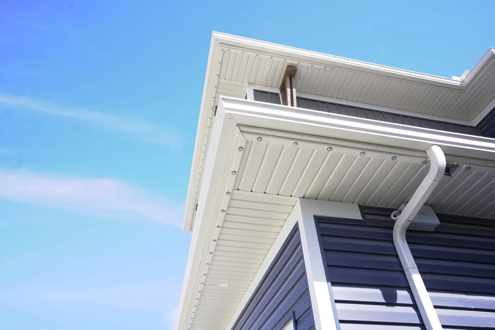 Daytime close-up of white soffit and fascia against a blue sky, the lighting track fitted so flush that only small evenly spaced lenses are visible.